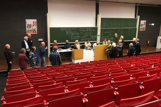 Twintig oud-bezetters staan in collegazaal KC-07, zingend